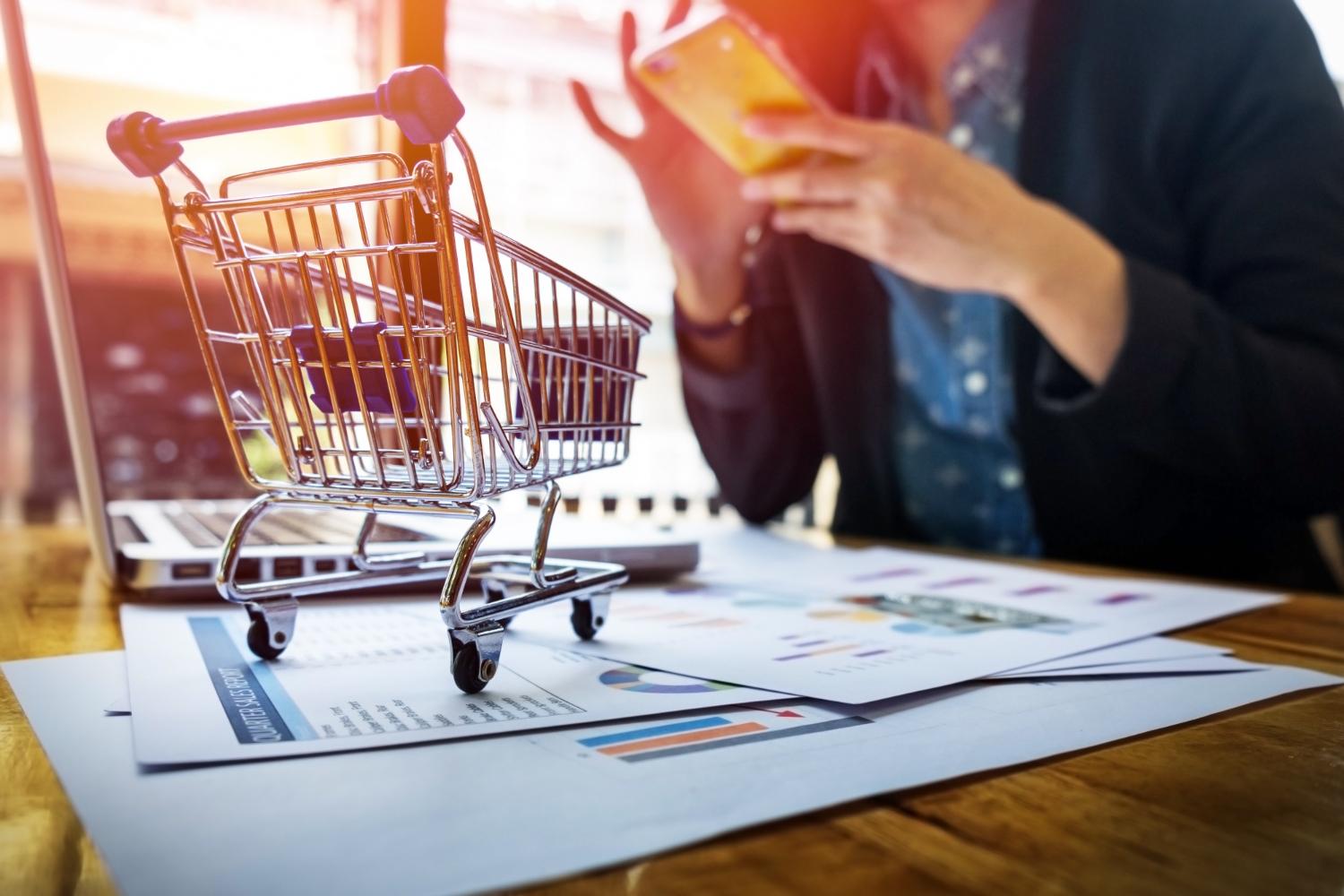 Contadora calculando impostos, com carrinho de compras em mesa simbolizando a tributação de e-commerce