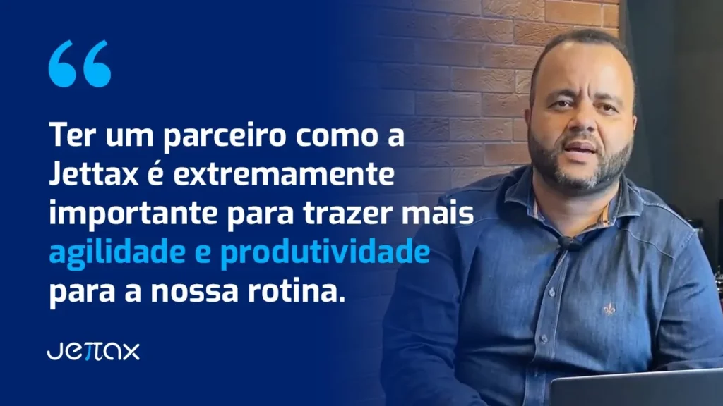 Homem sorrindo, usando camisa azul, em frente a uma parede de tijolos, falando sobre a importância da JetTax.