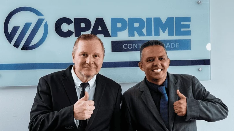 Dois profissionais da CPA Prime Contabilidade sorrindo e sinalizando positivo com o logo ao fundo, pela parceria.