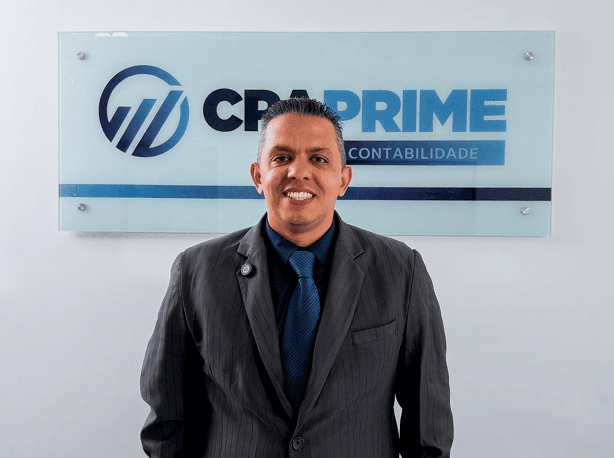 Thiago Wilsom da CPA Prime Contabilidade sorrindo em frente ao logo da empresa