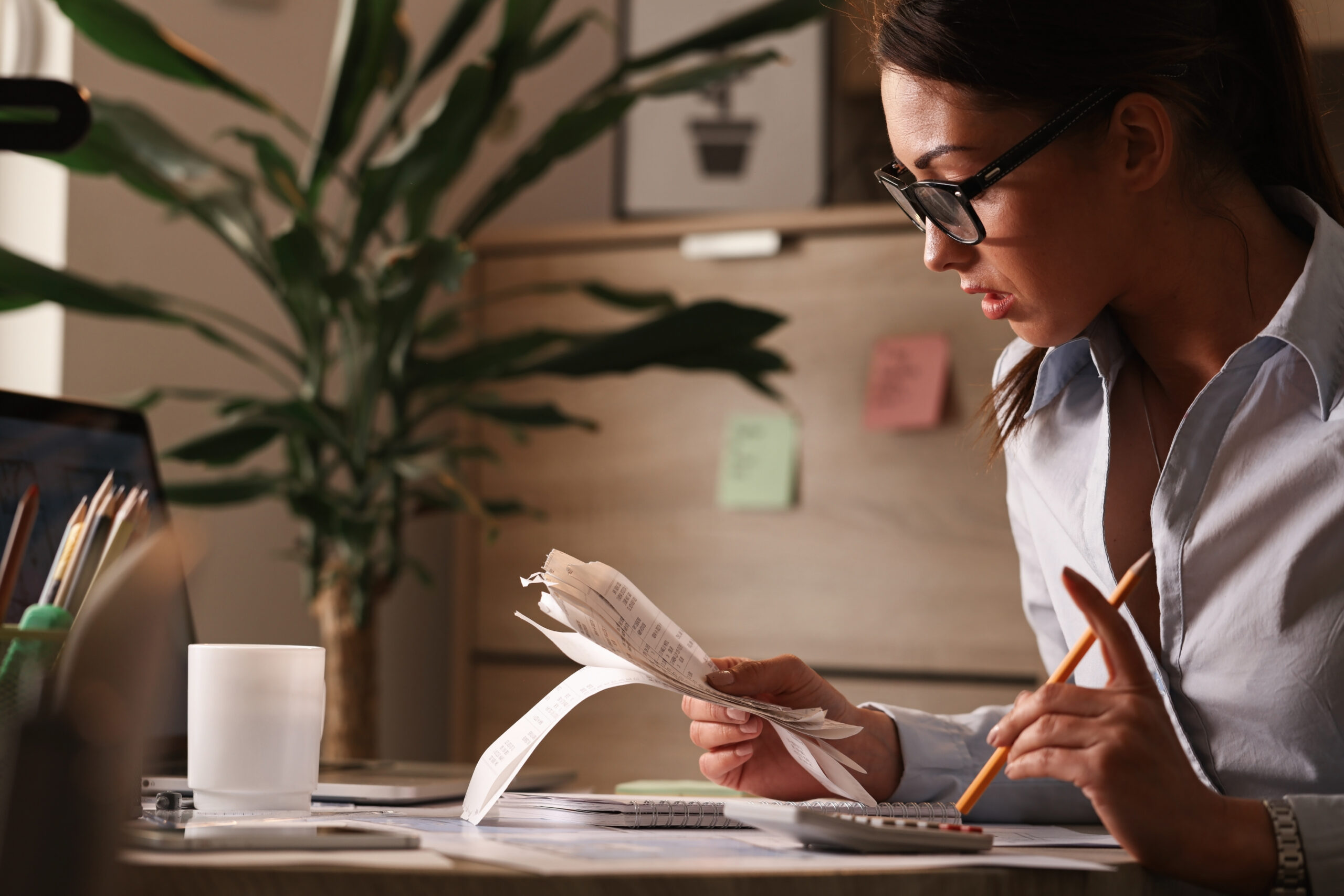 Profissional analisando comprovantes e documentos financeiros em uma mesa de trabalho, utilizando calculadora para conferência de informações.