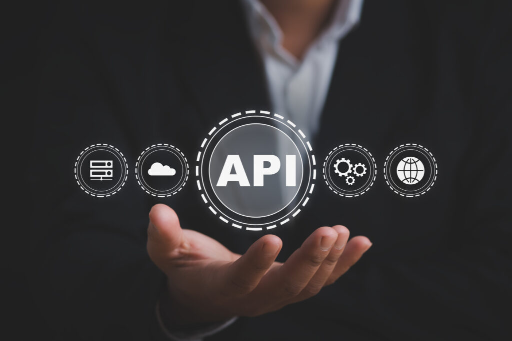 Mão aberta de um profissional de terno segurando um ícone digital com a sigla API, cercado por ícones de servidor, nuvem, engrenagens e globo.