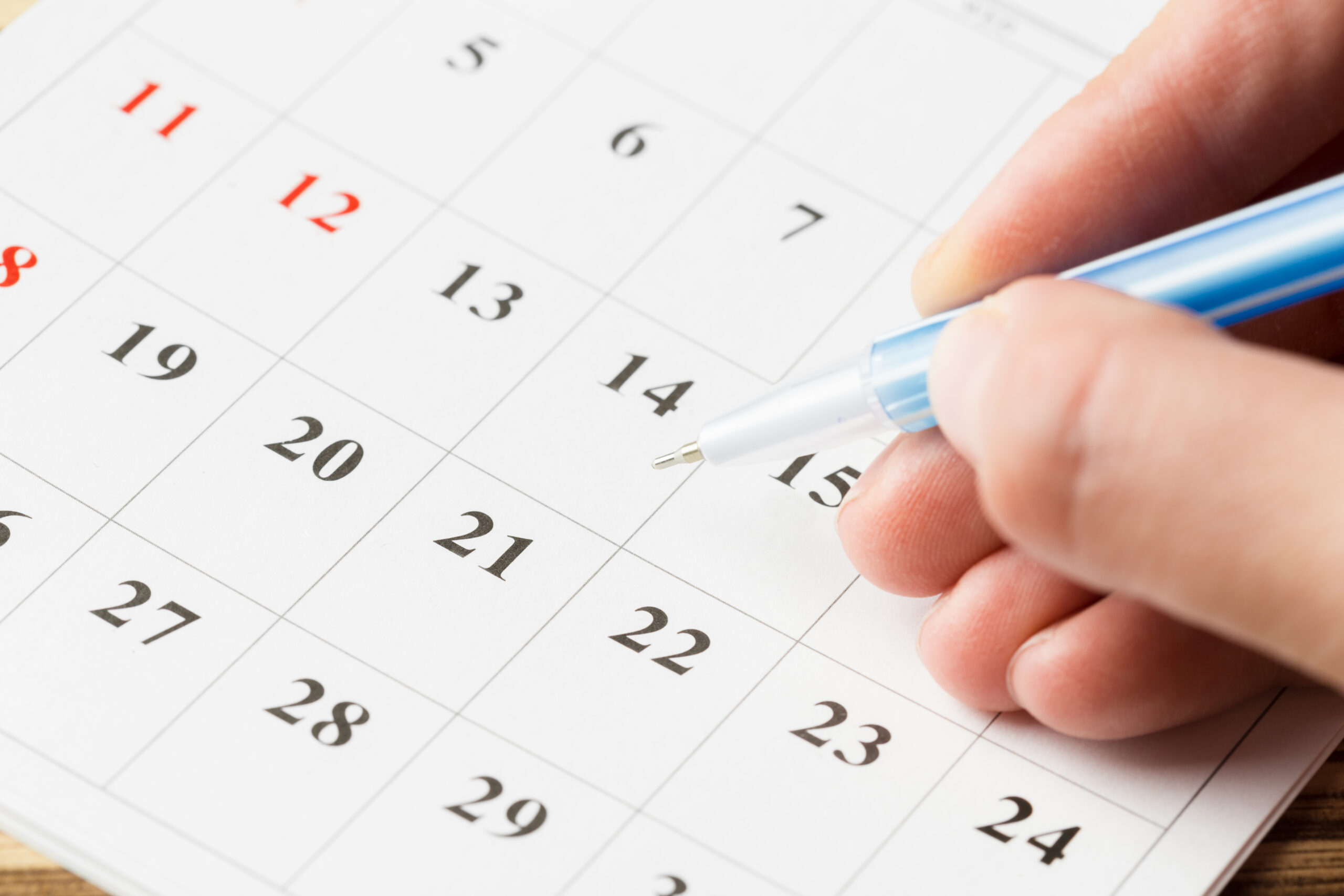 Mão segurando caneta azul sobre um calendário, apontando para o dia 15, representando a Agenda Tributária de outubro de 2026.
