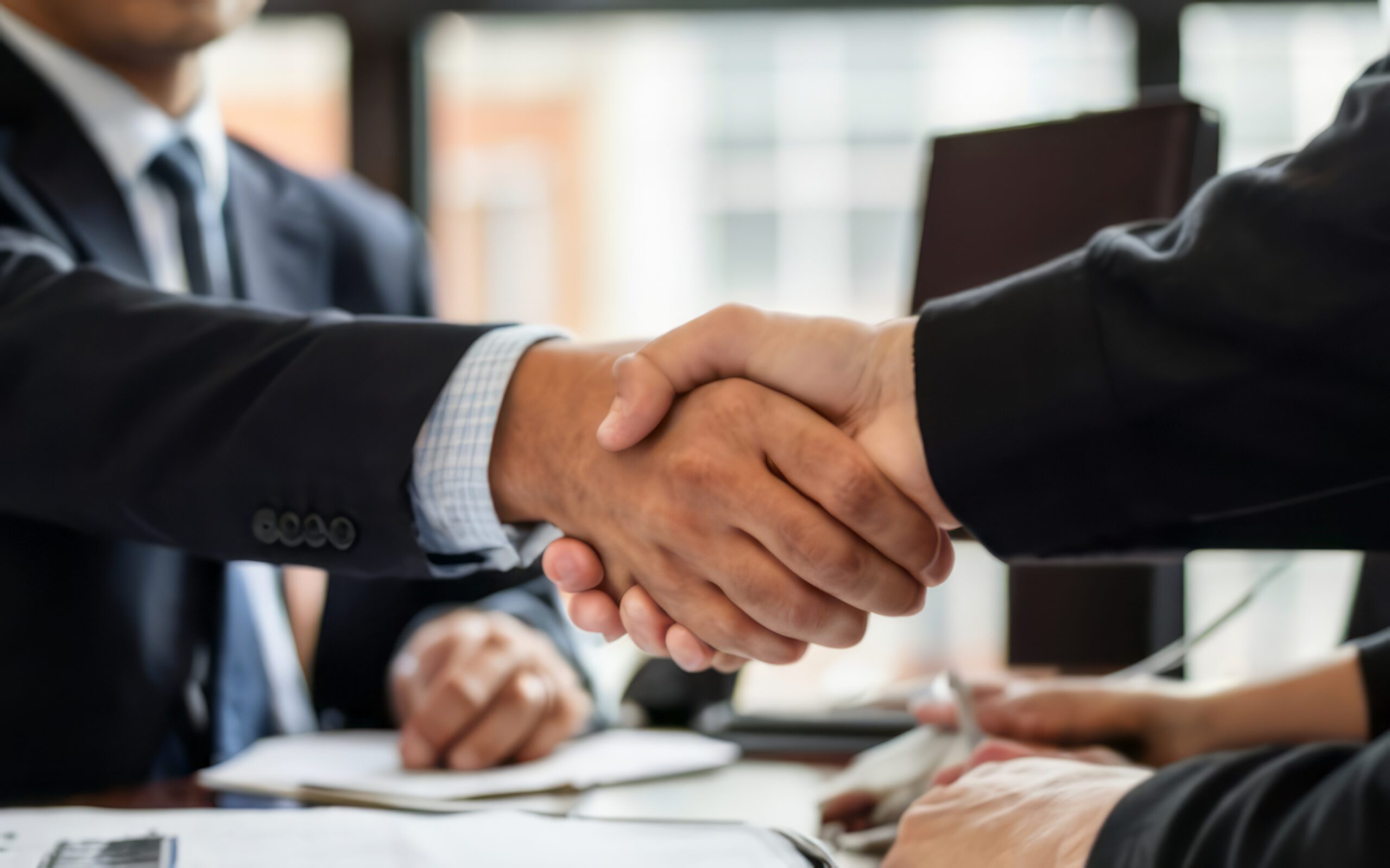Dois empresários de terno apertando as mãos em reunião de escritório, simbolizando acordo e parceria de negócios bem-sucedida