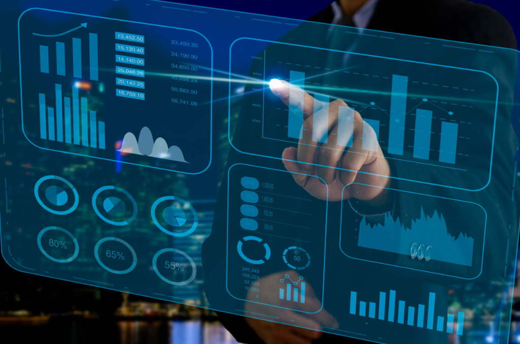 Profissional de terno toca um painel digital transparente com gráficos de barras, indicadores percentuais e dados financeiros, sobre um fundo noturno de cidade.