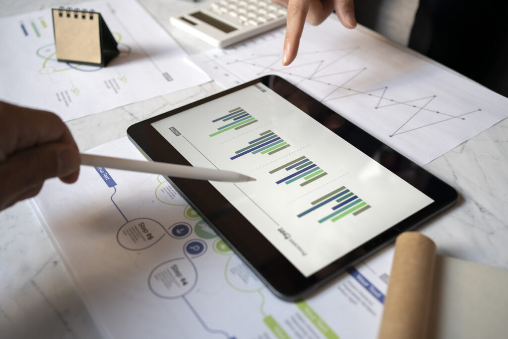 Contadores analisam gráficos de barras em um tablet, com relatórios impressos, calculadora e calendário sobre a mesa