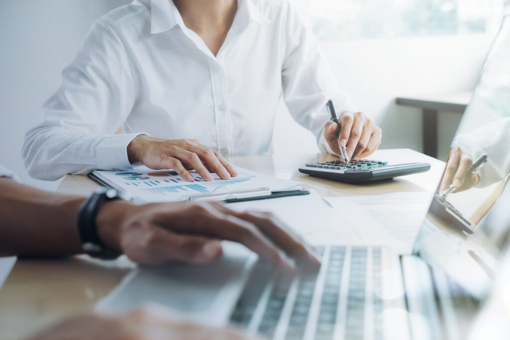 Contadores conferem relatório com gráficos usando calculadora e notebook durante a apuração fiscal no escritório