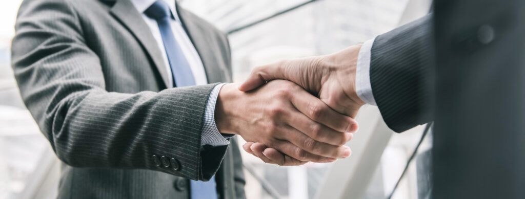 Dois profissionais de terno se cumprimentam com um aperto de mão em um ambiente corporativo.