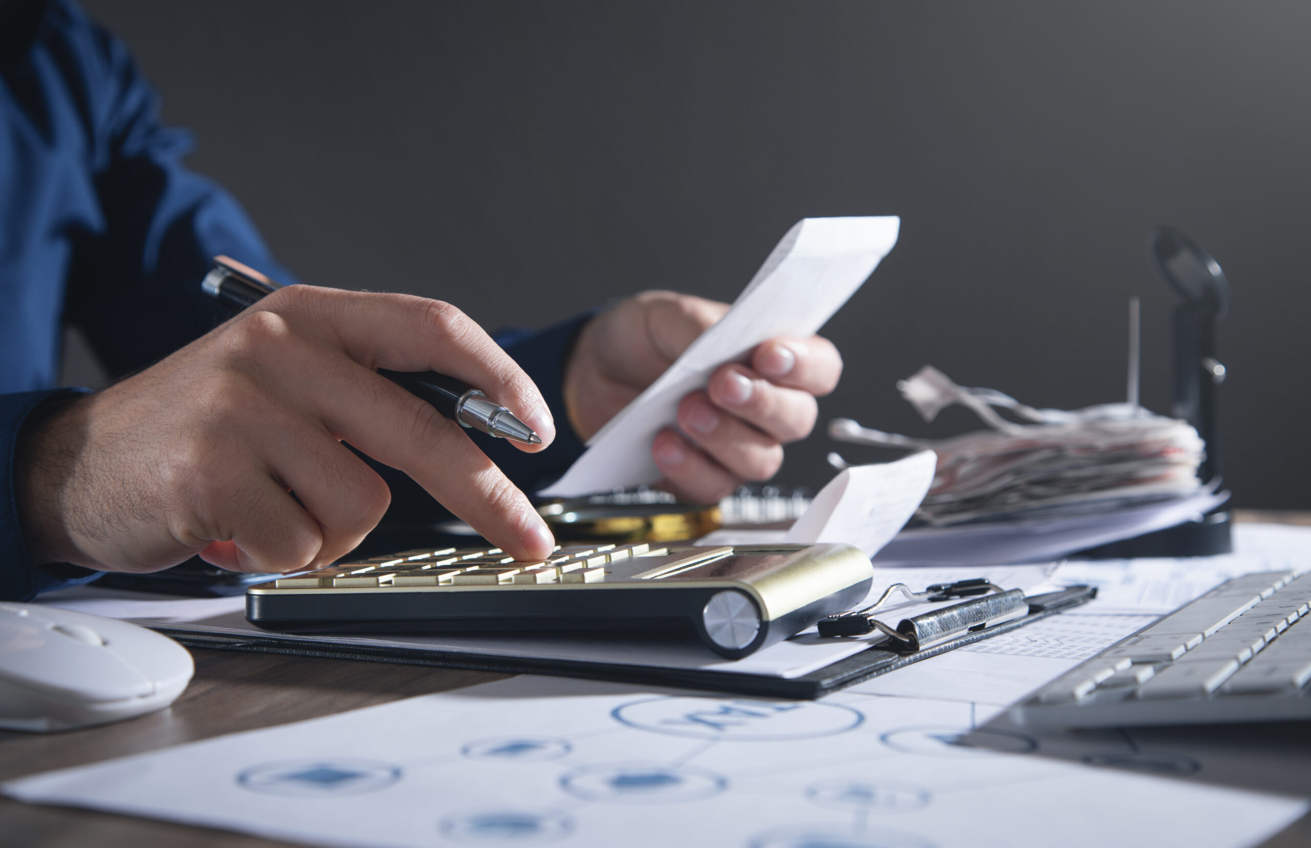 Contador conferindo cupom fiscal e digitando em calculadora sobre mesa com documentos, pasta de notas e diagrama de arquivos XML