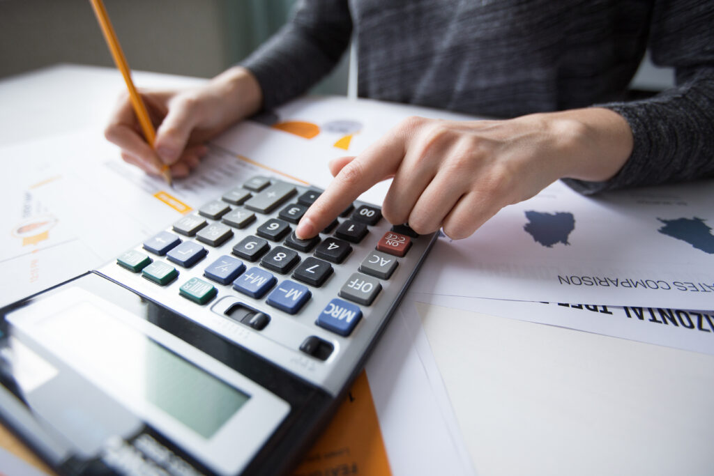 Profissional usando calculadora e fazendo anotações a lápis sobre relatórios impressos com gráficos.