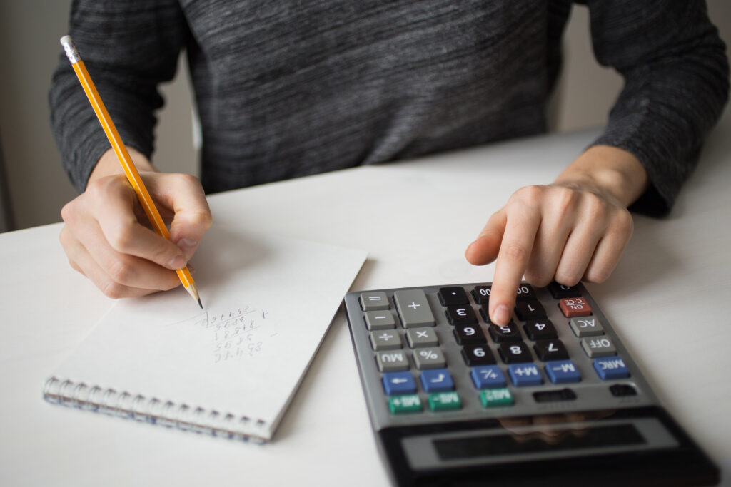 Pessoa faz contas em uma calculadora de mesa e anota os números em um bloco de papel com lápis