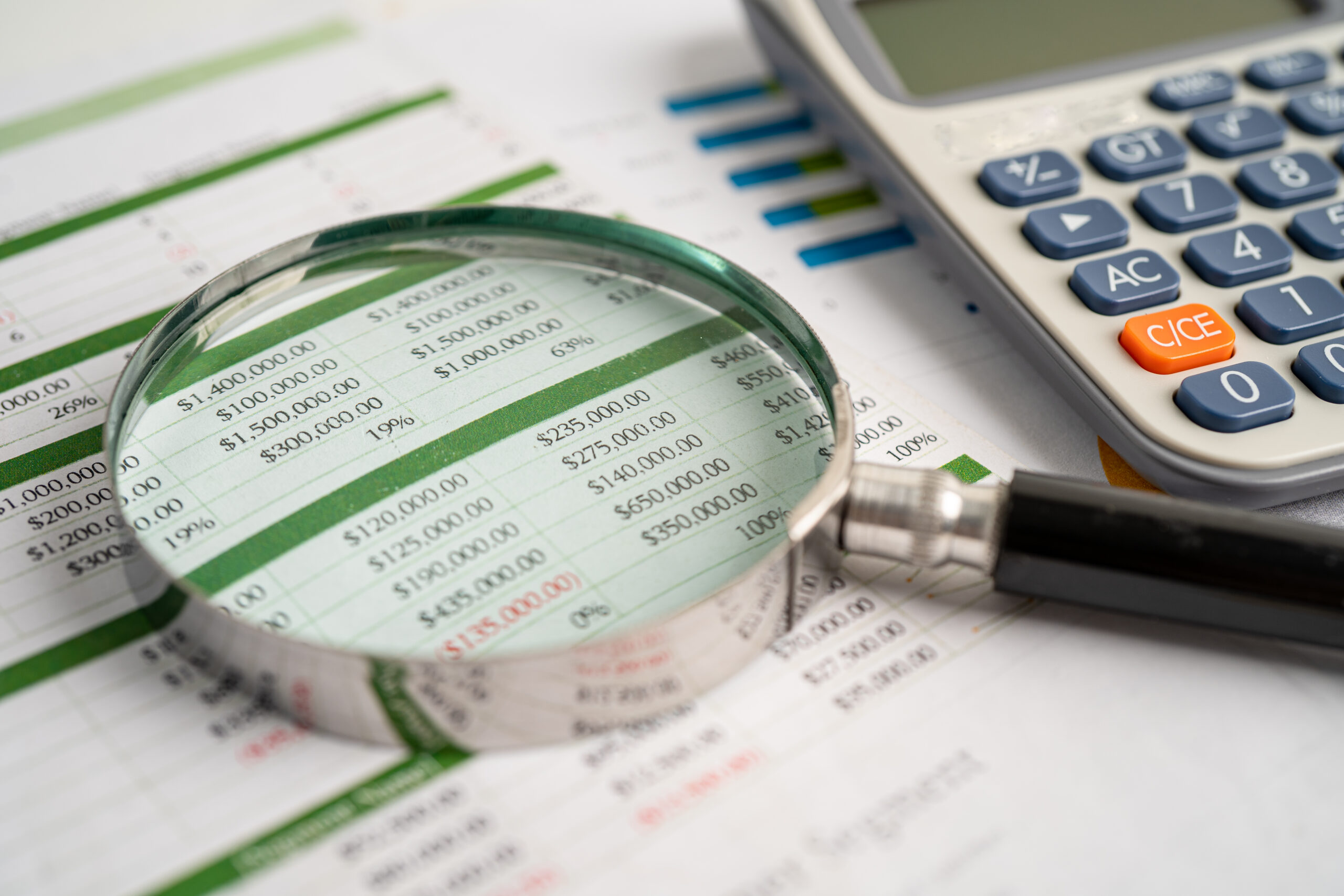 Lupa sobre uma planilha financeira ao lado de uma calculadora, representando análise e classificação tributária.