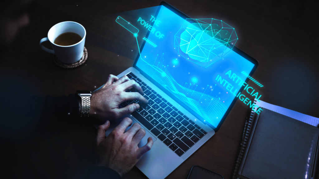 Pessoa digitando em um notebook sobre uma mesa escura, ao lado de uma xícara de café. Da tela saem gráficos luminosos em azul, com a ilustração de um cérebro digital e a frase “The power of artificial intelligenc